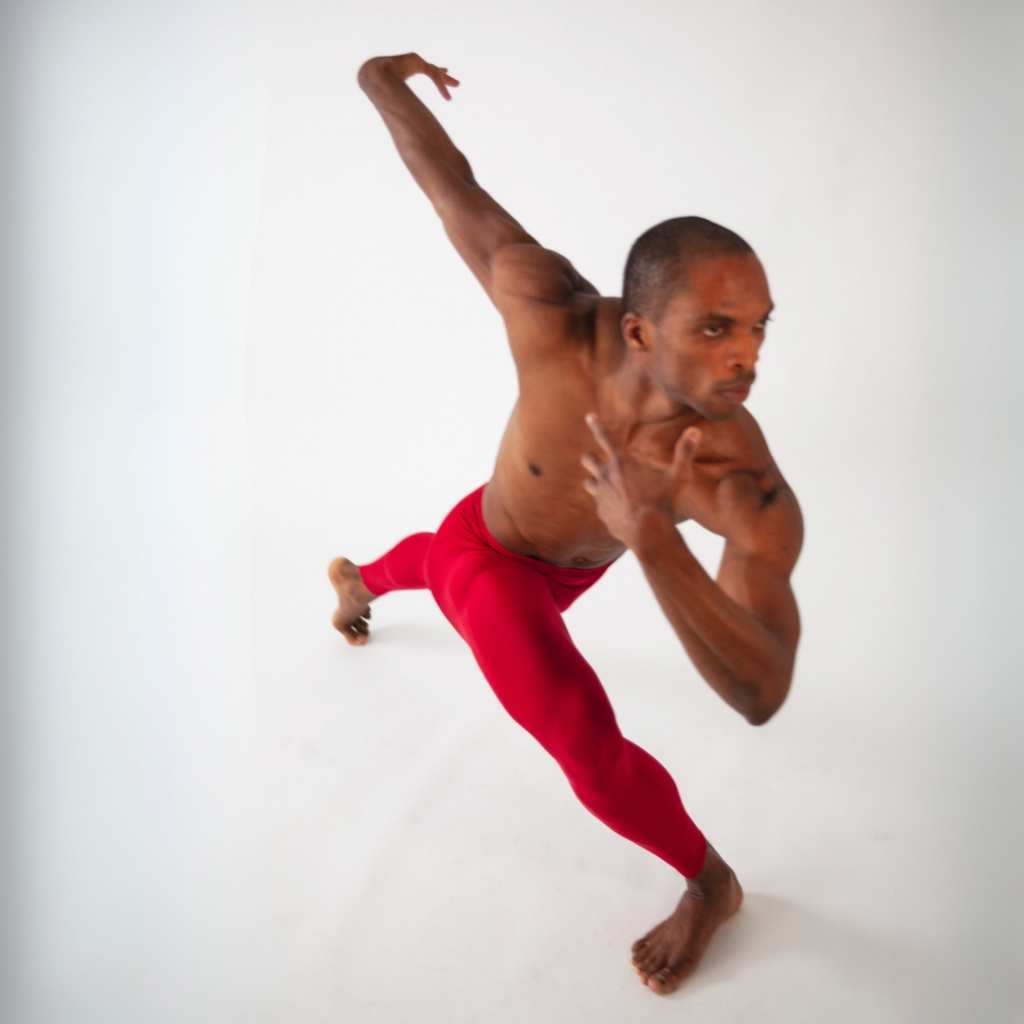 Male dancer in red focused in a pose, showing intentional focus and concentration.